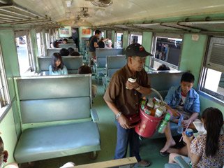 3rd class seats on a Thai train, with a vendor selling soft drinks & beer.